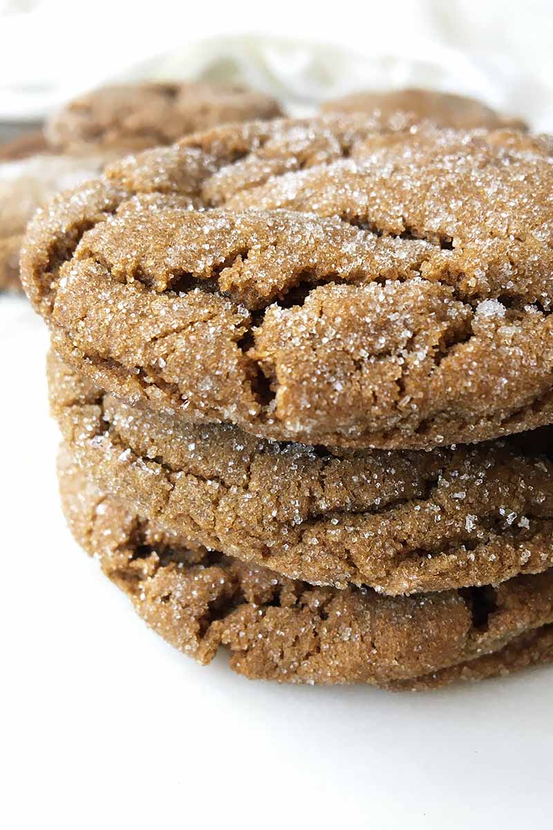 Vertical close-up image of a stack of crackled dark brown cookies coated in sugar.