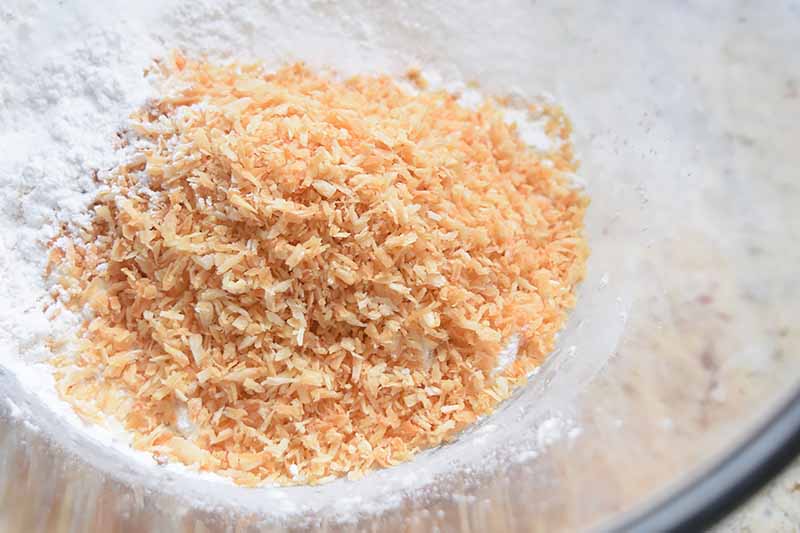 Horizontal image of toasted coconut flakes on top of other dry ingredients.