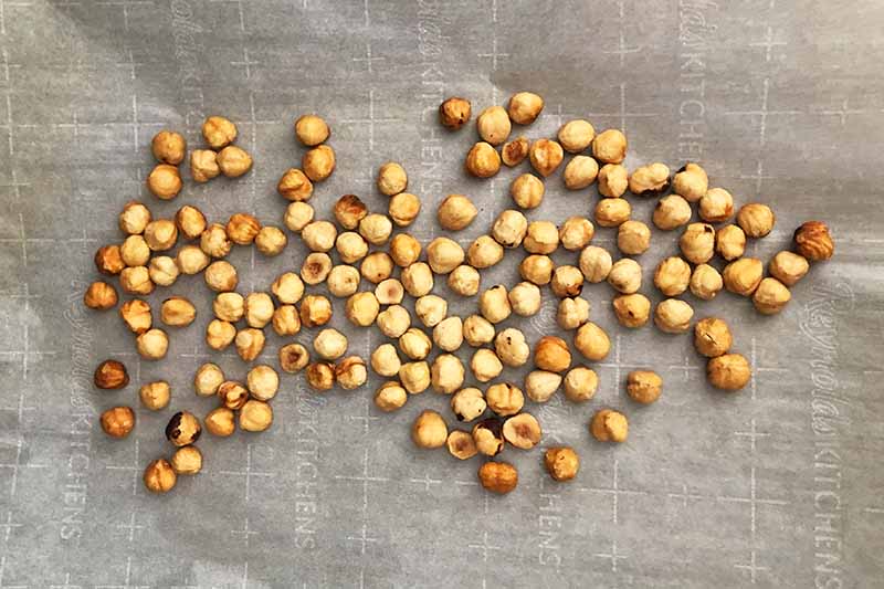 Horizontal overhead image of toasted hazelnuts on a piece of parchment paper on top of a baking sheet.