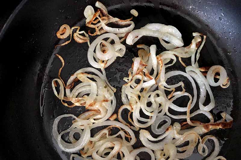 Horizontal overhead closely cropped image of thinly sliced onion sauteeing in a nonstick frying pan.