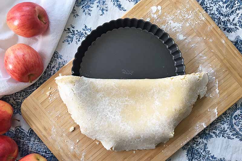 Horizontal image of a folding piece of dough on top of an empty metal pan.