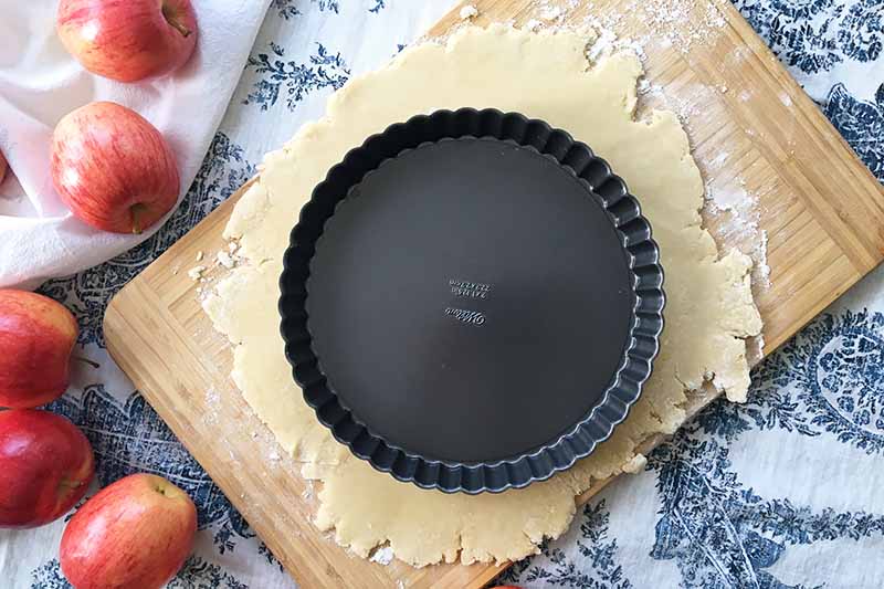 Horizontal image of an empty tart pan on top of rolled out pie dough.