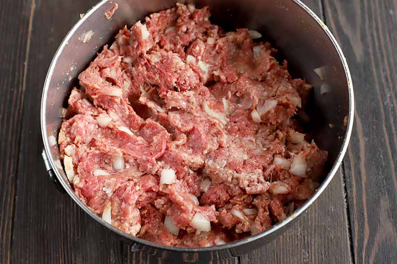 Horizontal image of a raw ground beef mixture in a metal bowl.