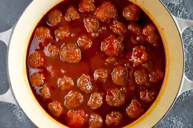 Horizontal top-down image of meatballs in a red liquid mixture in a pot.