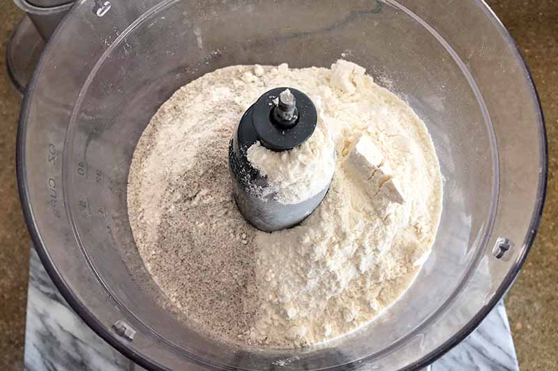 Horizontal overhead image of flour in a food processor, on a brown surface.