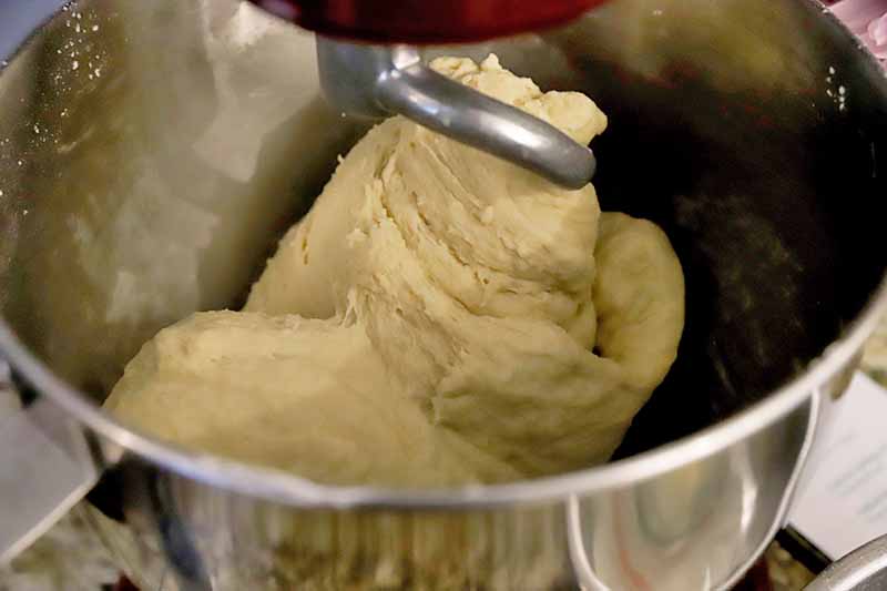 Horizontal image of kneading dough in a mixing bowl fitted with the dough hook attachment.
