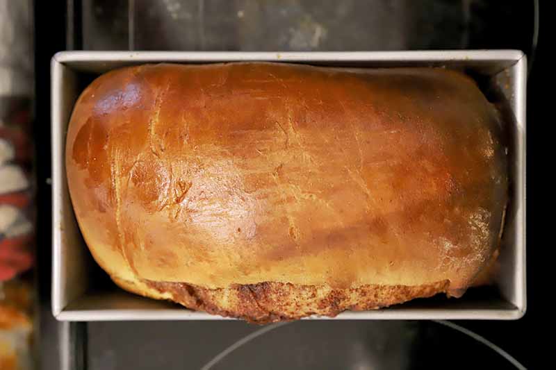 Horizontal image of a browned baked loaf in a metal rectangular pan.