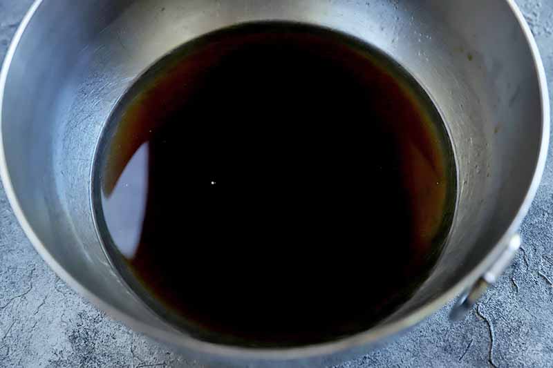 Horizontal image of a metal bowl with dark liquid.