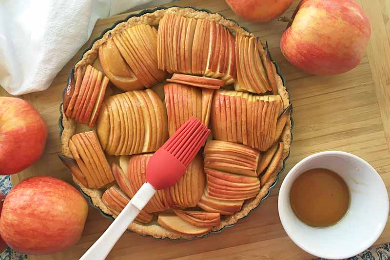 Horizontal image of glazing a whole fruit pastry in syrup with a red pastry brush.