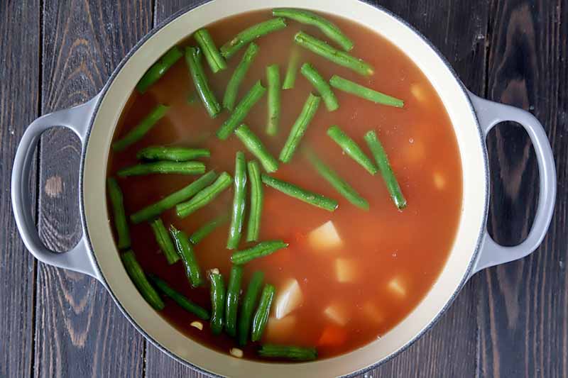 Horizontal image of a pot with green beans and a red liquid.