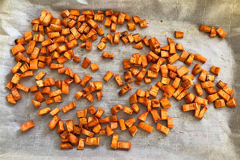Horizontal image of roasted cubed sweet potato on a piece of parchment paper.