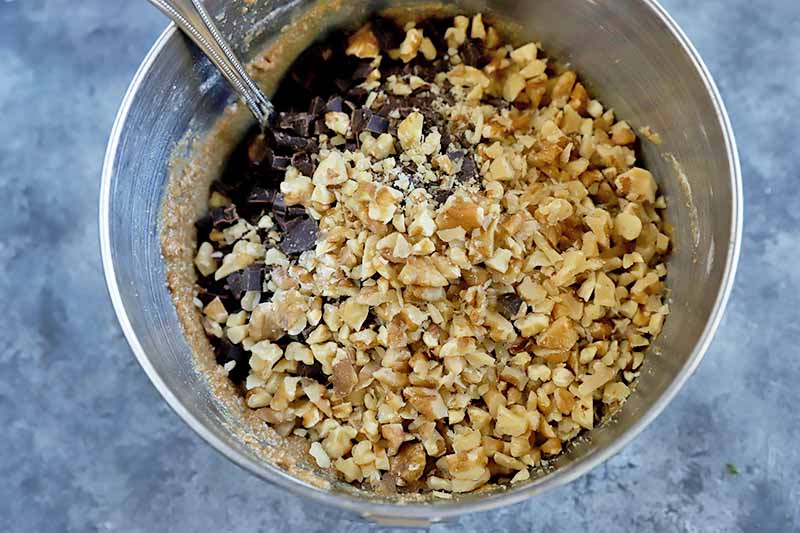 Horizontal image of mixing chopped walnuts into wet and dry ingredients in a metal bowl.