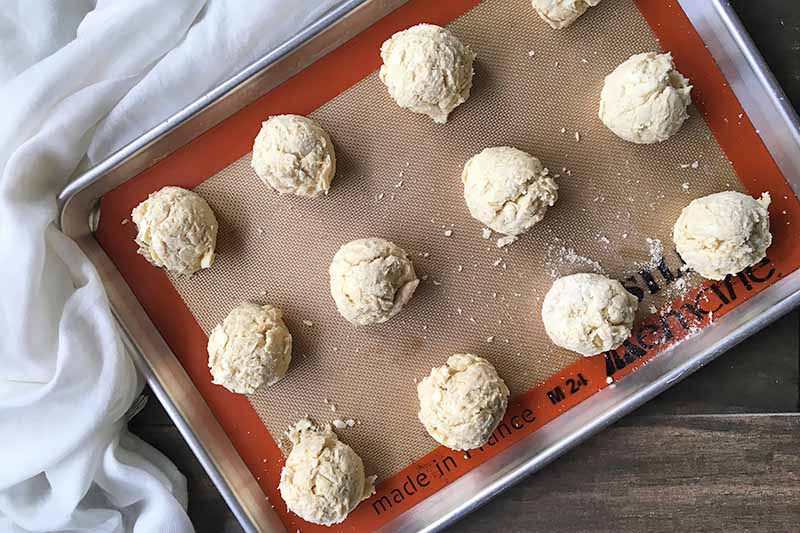 Horizontal image of a baking sheet with round mounds of light dough on top.