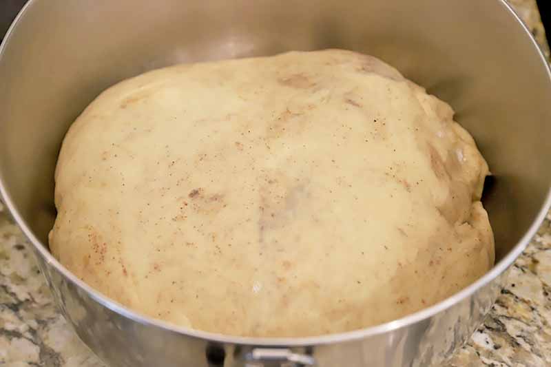 Horizontal image of a risen spiced dough in a metal mixing bowl.