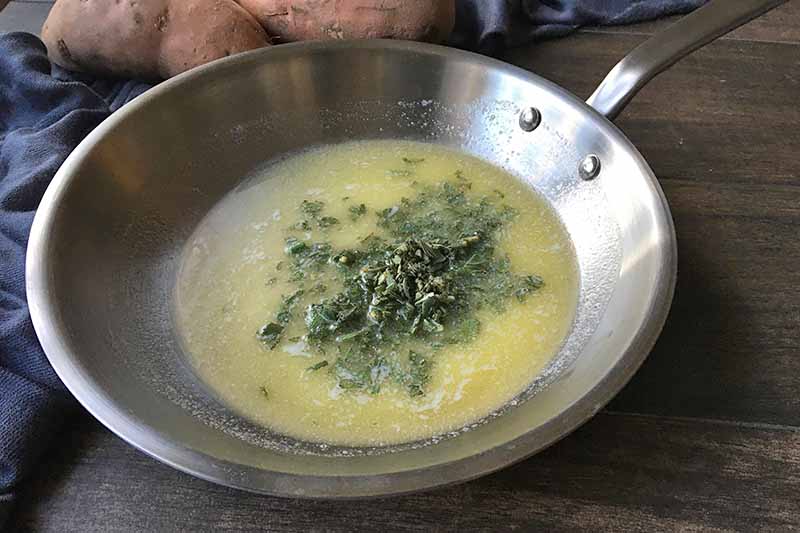 Horizontal image of a pan with melted butter and chopped sage.