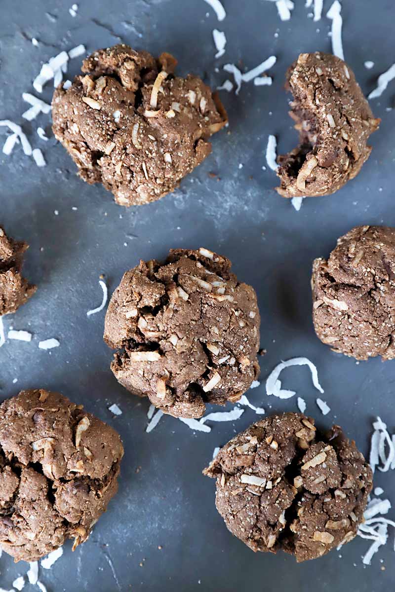 Vertical overhead image of chocolate cookies on a gray surface, with scattered shreds of coconut.
