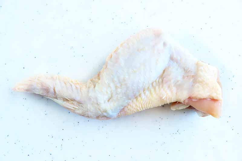 Horizontal image of one whole poultry wing on a white surface.