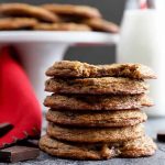 Horizontal image of a stack of thin, dark cookies next to a red towel and white cake stand.