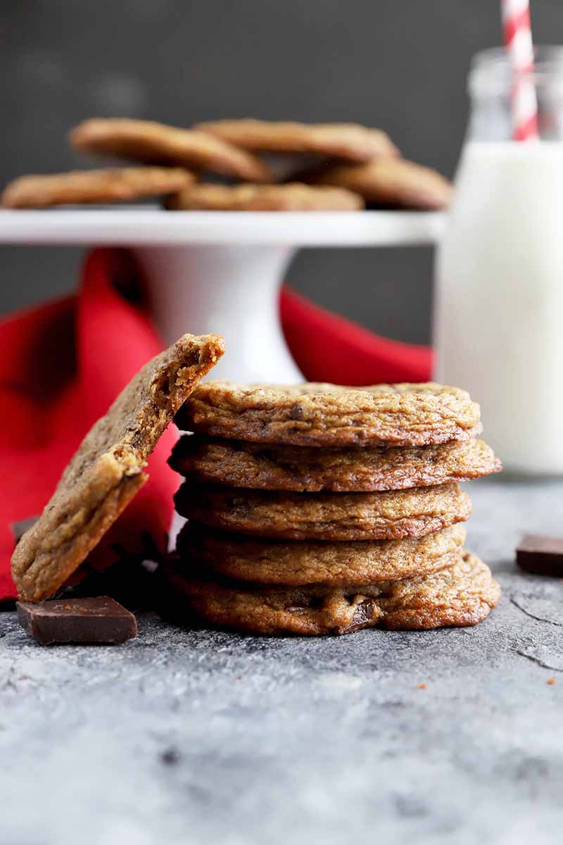 Vertical image of a stack of cookies, and one on the side with a bite taken out of it, in front of a red towel.