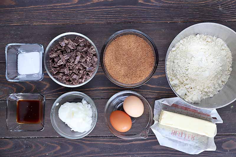 Horizontal image of assorted dry ingredients, wet ingredients, butter, and eggs in various bowls.