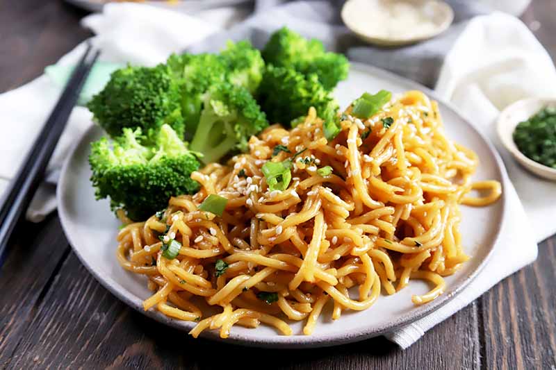 Horizontal image of a white dish with pasta with a brown sauce next to broccoli florets.