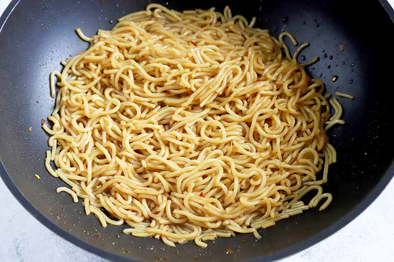 Horizontal image of a wok with spaghetti and sauce.