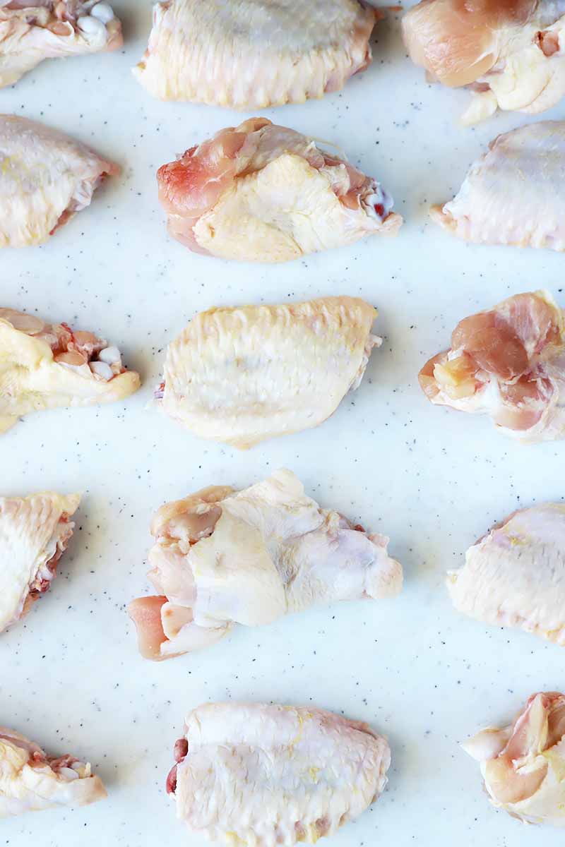 Vertical image of raw poultry parts neatly arranged on a white cutting board.