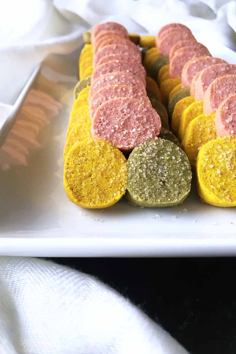 Vertical image of two rows of neatly arranged treats with three colors sprinkled with sugar on a white platter.