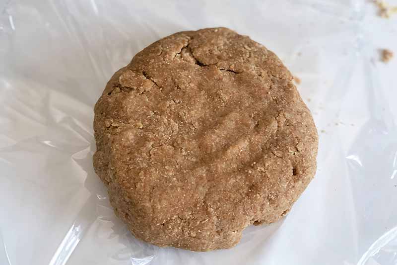 Horizontal image of a mound of dark brown dough on plastic wrap.