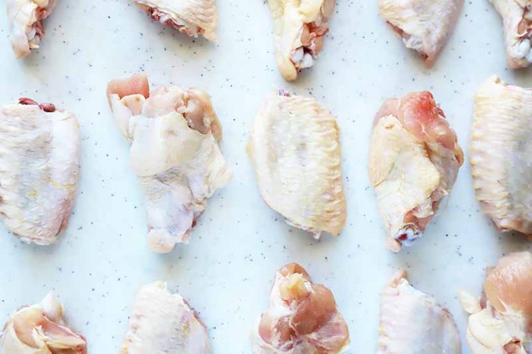 Horizontal image of raw poultry parts neatly arranged in rows on a white cutting board.
