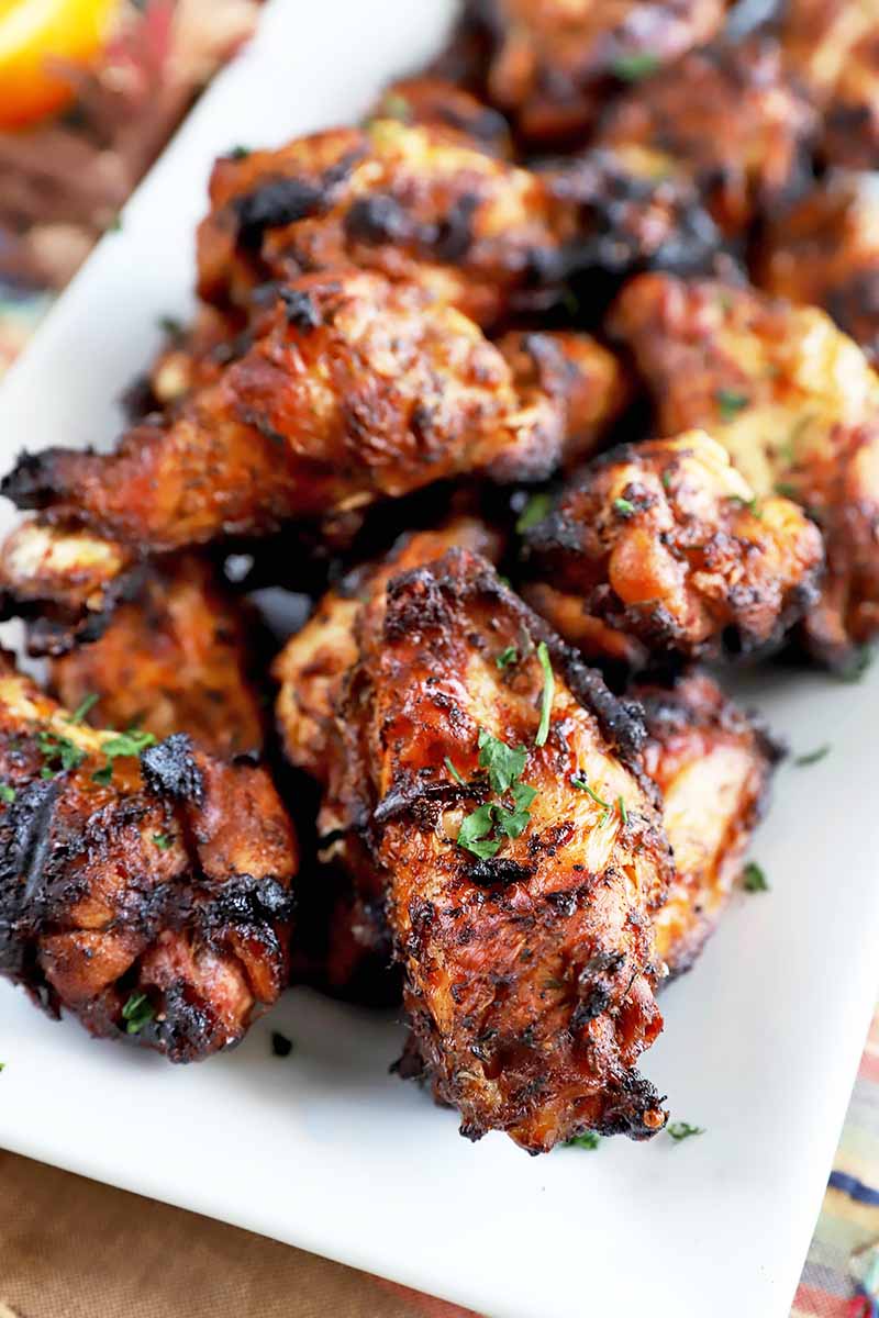 Vertical image of a white platter of grilled chicken wings, selective focus.