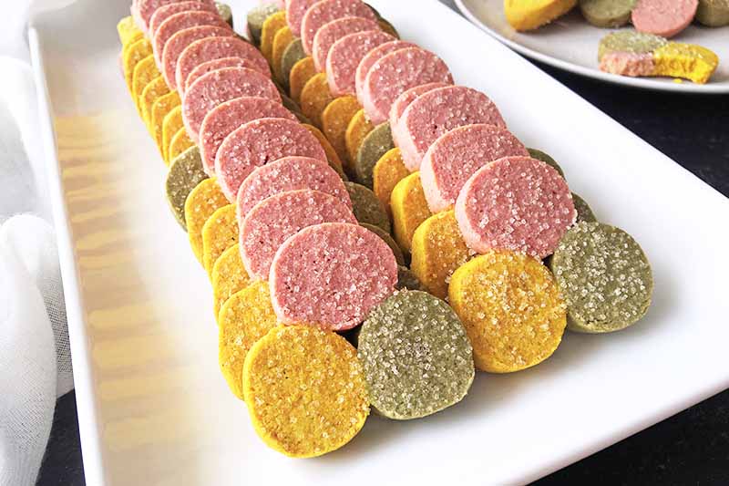 Horizontal image of two rows of neatly stacked colored cookies on a white dish.
