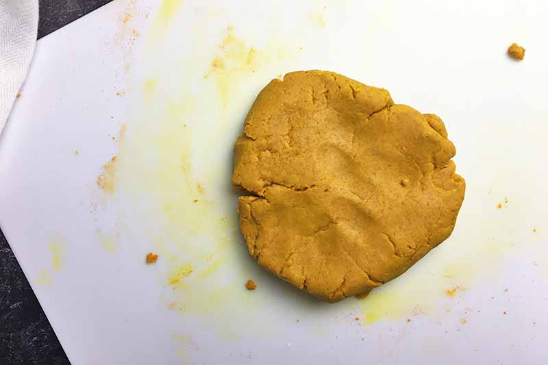 Horizontal image of a yellow disc of dough on a white cutting board.