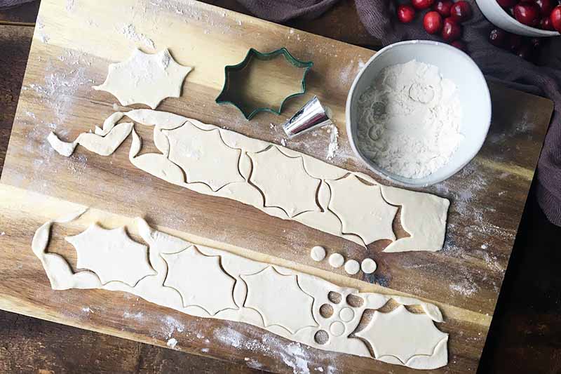 Horizontal image of a wooden cutting board with decorations cut out in strips of dough on a wooden cutting board with flour.