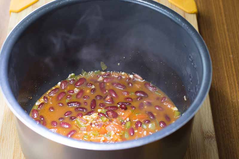 Horizontal image of a black pot with a mixture of liquid, beans, and vegetables.