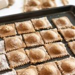 Horizontal image of a baking sheet with rows of a filled square pasta.