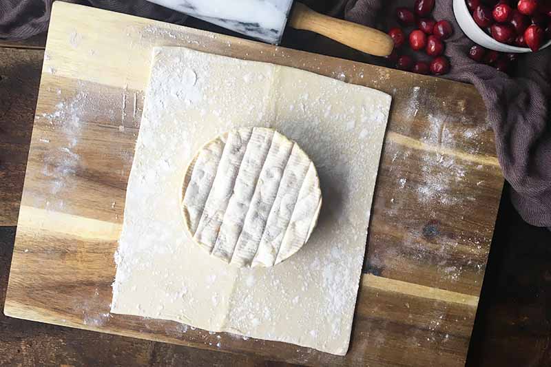 Horizontal image of a square piece of dough with brie in the middle on a floured wooden cutting board.