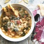 Horizontal image of a bowl of soup with cannellini and escarole on a red checkered towel.