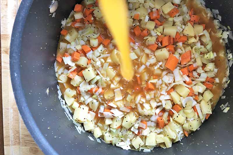 Horizontal image of stock pouring into a pot with cooked diced vegetables.