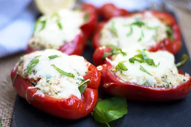 Horizontal image of stuffed red vegetables with cheese on a slate.