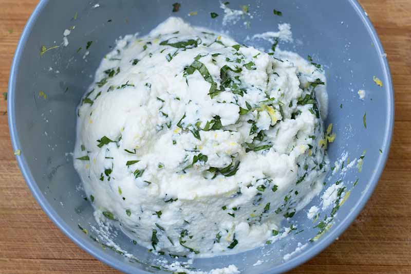 Horizontal image of a ricotta and herb filling mixed in a bowl.