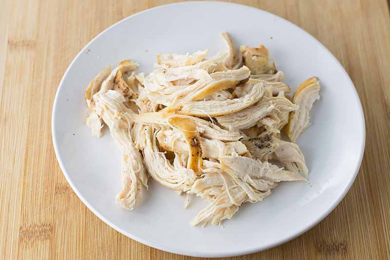 Horizontal image of a white plate with shredded cooked poultry.