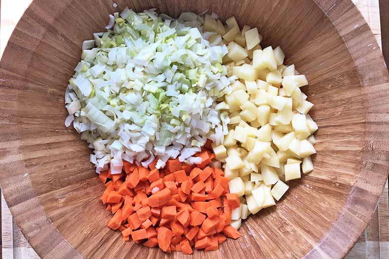 Horizontal image of diced potatoes, carrots, and leeks in a wooden bowl.