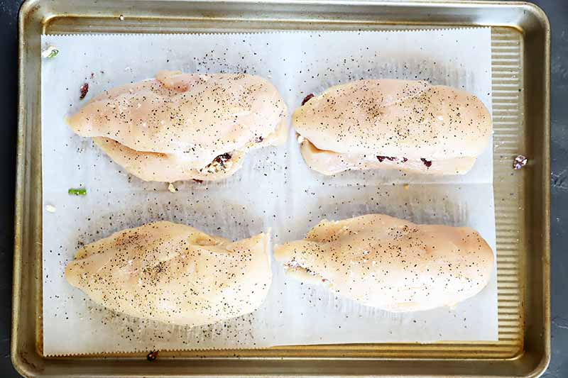 Horizontal image of four raw breasts with a filling on a baking sheet lined with parchment paper.