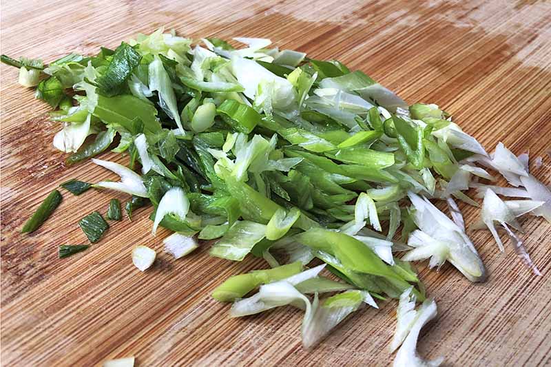 Horizontal image of finely chopped green onions on a wooden cutting board.