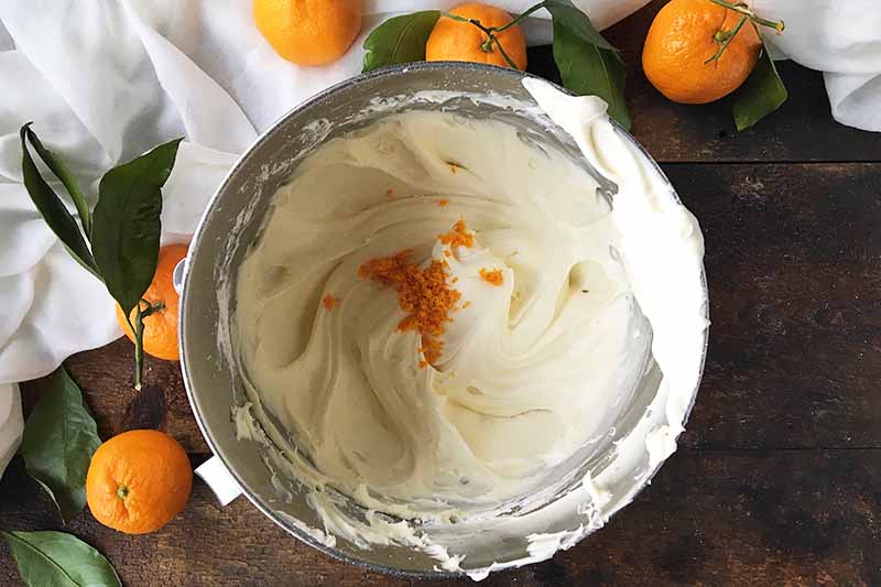 Horizontal image of a metal bowl with a thick and fluffy white icing and zest.