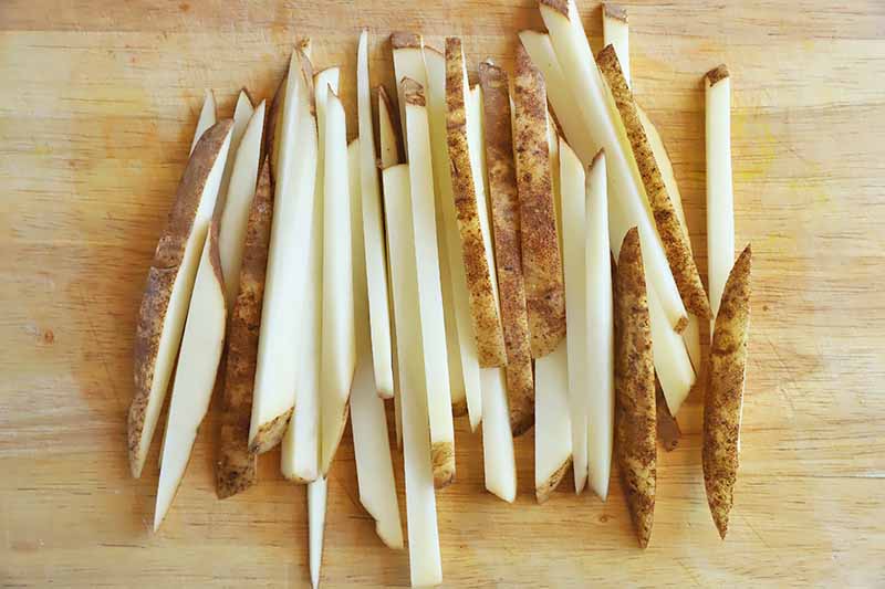 Horizontal image of matchstick slices of potatoes on a wooden board.