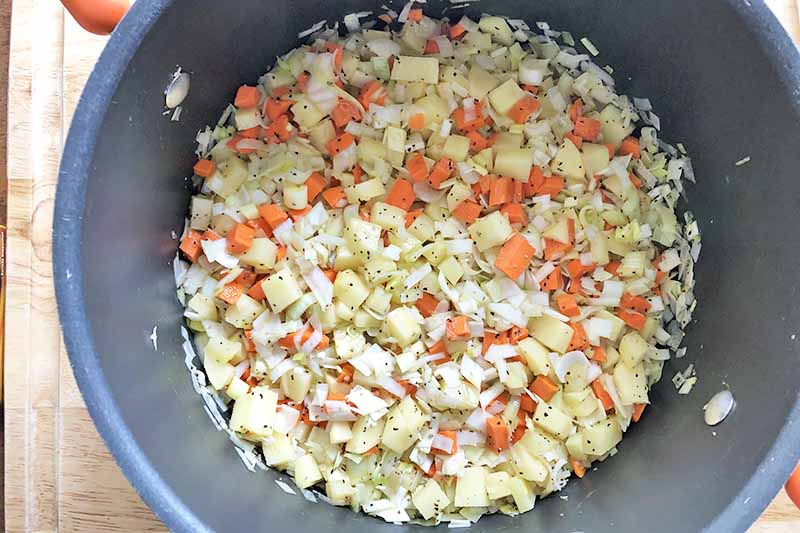 Horizontal image of cooking assorted diced and seasoned vegetables in a pot.