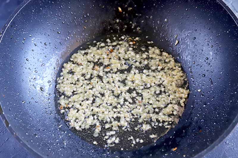 Horizontal image of cooking finely chopped garlic and ginger in oil in a wok.