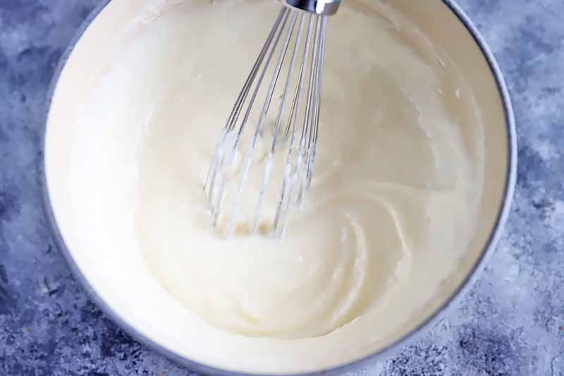 Horizontal image of whisking together a mornay sauce in a pot.